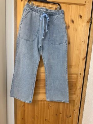 Ljusblåa loose fit jeans med dragsko - Säljer ett par ljusblåa loose fit jeans med breda ben och elastisk midja med blå dragsko. Jeansen har stora framfickor och bakfickor, samt avslappnad passform. 