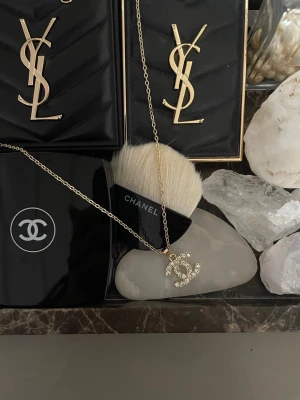  halsband  - Guldigt halsband med klassisk CC-logga dekorerad med gnistrande strass. Tunn kedja i guldfärg och elegant hängsmycke som ger en lyxig känsla. Perfekt för dig som gillar exklusiva accessoarer och vill sticka ut med en ikonisk detalj.