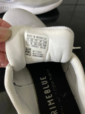 Vita Adidas Primeblue sneakers - Snygga vita Adidas Primeblue sneakers med blå detaljer och klassiska tre ränder på sidan. Ovandelen är i mesh för bra andningsförmåga och sulan är tjock och greppvänlig. Skorna har snörning och Adidas-logga på hälen. Perfekta för en sportig och modern stil.