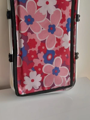 Stor isolerad picknickkorg - 30L kylväska med retromotiv - Denna bärbara kylväska på 30 liter är perfekt för familjeutflykter, stranddagar eller matinköp. Den har ett fantastiskt retroblommigt 70-talstryck i varma hösttoner (orange, gult och brunt).  Viktiga funktioner: Stor kapacitet: 30 liter (gott om plats för drycker, snacks och lunch). Isolerad insida: Håller mat och dryck svala eller varma i timmar.  Robust design: Lätt aluminiumram med ett bekvämt vadderat handtag.  Mått: 40 cm xx 23 cm x 30 cm (ca 15,7" x 9,05" x 11,8").
