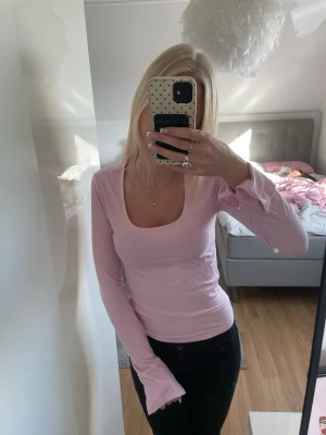 Ljusrosa långärmad topp med slits - Ljusrosa långärmad topp med rundad, djup ringning och slitsar vid ärmsluten. Toppens passform är tight och materialet känns mjukt och stretchigt. Perfekt att styla med jeans eller kjol. Använt 2 gånger!