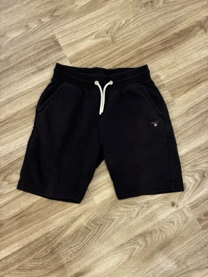 Mörkblå  shorts från Gant med snörning - Mörkblå shorts från Gant med vit snörning i midjan och två sidofickor. Klassisk och enkel design med liten Gant-logga på vänster ben. Perfekta för sommaren och tillverkade i mjukt bomullsmaterial. nypris (719)