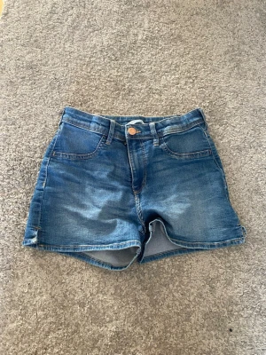 Blå jeansshorts från H&M - Snygga blå jeansshorts från H&M med klassisk femficksdesign och gul kontrastsöm. Shortsen har en bekväm passform och är tillverkade i denim med lätt tvättad look. Perfekta för sommardagar och enkel att matcha med olika toppar.
