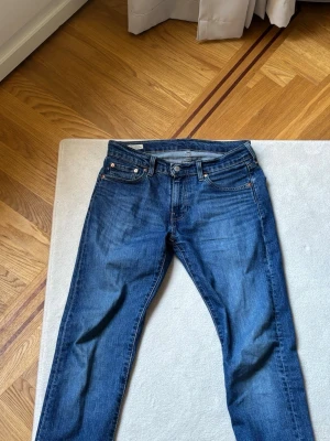 Levi's blå raka jeans - Klassiska blå jeans från Levi's med rak passform och fem fickor. Jeansen har en snygg mellanblå tvätt och detaljer i kopparfärgad metall. Tillverkade i slitstark denim av bomull. Perfekta för en avslappnad och tidlös stil.