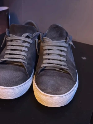 Mörkgrå mockasneakers med vit sula - Snygga mörkgrå sneakers i mocka med matchande grå skosnören och vit, klassisk gummisula. Låg modell som passar perfekt till jeans eller chinos. Minimalistisk design utan synliga loggor för en clean look.