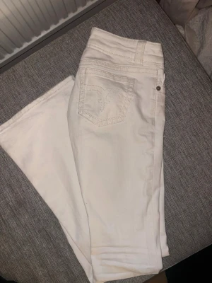 Vita raka jeans från Ginatricot - Säljer ett par vita jeans från Ginatricot med bootcut som passform och klassisk femficksdesign. Jeansen har broderad detalj på bakfickan och silverfärgade nitar. Tillverkade i ett mjukt bomullsmaterial med lite stretch för extra komfort.