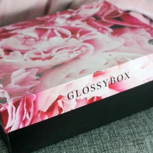Glossybox presentask - Säljer en snygg presentask från Glossybox med blommigt lock i rosa nyanser och svart botten. Insidan är dekorerad med rosa loggor på svart bakgrund. Perfekt för förvaring eller som presentlåda.