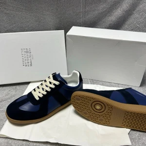 Blå Maison Margiela sneakers- 22- Strl 42 - Snygga sneakers från Maison Margiela i blå mocka och läder med vita snören och klassisk gummisula. Modellen har en stilren och tidlös design med mörkblå paneler och diskret branding på tungan. Perfekta för dig som gillar exklusiva och trendiga  skor. Kom dm för mer info, storlek 42 och dem är helt nya, oanvända🥂