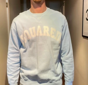 Ljusblå sweatshirt DSQUARED - Ljusblå sweatshirt från DSQUARED med broderad logga i vitt framtill. Tröjan har rund halsringning, långa ärmar och ribbade muddar vid ärmslut och nederkant. Perfekt för en avslappnad och stilren look.