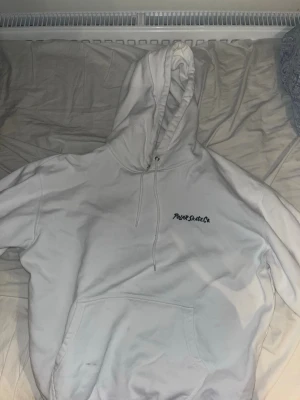 Vit hoodie från Polar Skate Co - Säljer en vit hoodie från Polar Skate Co med svart logga på bröstet och en stor, färgglad grafisk design i blått, orange och grönt på ryggen. Hoodien har huva med dragsko och en stor magficka. Perfekt för dig som gillar streetwear och unika prints. Nypris 800kr