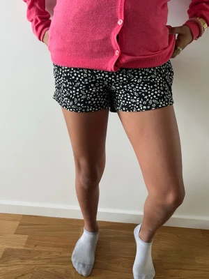 Svartvit blommig skort - Supersöt svart skort med vitt blommönster. Skorten har en kjol framtill och shorts baktill, vilket gör den både snygg och bekväm. Perfekt för dig som gillar en lekfull och trendig stil. Materialet känns lätt och luftigt.