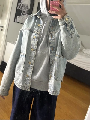 Jeansjacka Zara  - Snygg oversized jeansjacka i ljusblå denim med klassiska guldiga knappar och två stora fickor framtill. Jackan har en avslappnad passform och raka ärmar, perfekt för en cool och avslappnad stil.