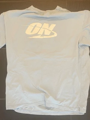 Ljusblå ON t-shirt med tryck - Säljer en ljusblå t-shirt från ON med stort vitt tryck på bröstet. Klassisk passform och rund halsringning. Perfekt för dig som gillar enkel och clean stil.