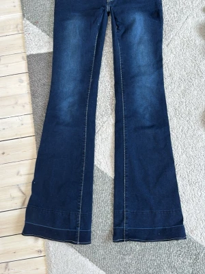 Mörkblå utsvängda jeans - Snygga mörkblå jeans med utsvängda ben och markerade sömmar. Klassisk femficksmodell med kontrastsömmar och lätt tvättade detaljer på låren och bak. Perfekta för dig som gillar retrostil och vill sticka ut med en trendig siluett. Har en liten fläck men den syns inte så bra. Jag har sytt dom mera lågmidjade själv och jag är inte så proffsig.