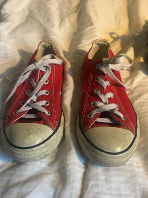 Röda låga sneakers med vita detaljer - Klassiska röda sneakers med vit gummitå och vita snören. Skorna har en låg profil och är tillverkade i canvas med vita sömmar och metallhål för snörningen. Yttersulan är vit med svart rand. Perfekta för en avslappnad och cool stil.