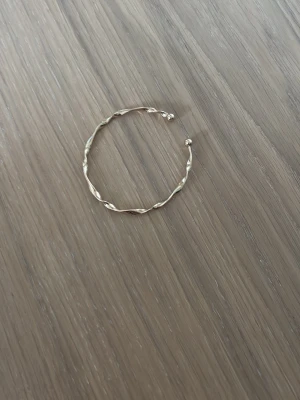 Tunt tvinnat guldarmband - Snyggt och minimalistiskt armband i guldfärgad metall med tvinnad design och små kulor vid öppningen. Perfekt för dig som gillar stilrena accessoarer med en twist.