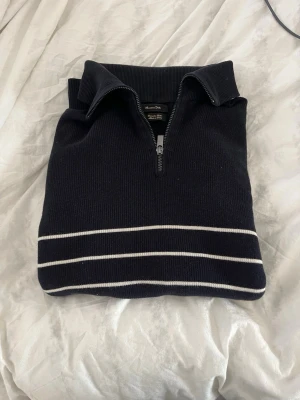 Mörkblå stickad tröja Massimo Dutti - Mörkblå stickad tröja från Massimo Dutti i extrafin bomull. Tröjan har halv dragkedja, hög krage och vita ränder nedtill. Perfekt för en stilren och avslappnad look.