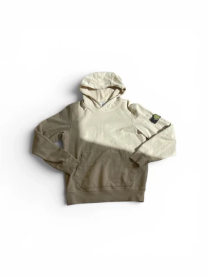 Beige hoodie från Stone Island Junior - Snygg beige hoodie från Stone Island Junior med klassisk huva och känguruficka framtill. Ikonisk logopatch på vänster ärm. Tillverkad i mjukt bomullsmaterial som är skönt att ha på sig. Perfekt för en avslappnad och trendig stil.