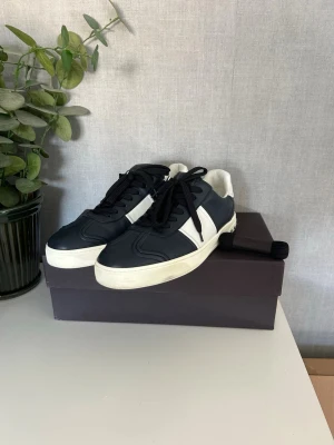 Valentino flycrews  - Snygga sneakers från Valentino i mörkblått och vitt läder med svarta skosnören. Klassisk låg modell med vit sula och dekorativa nitar baktill. Perfekta för dig som gillar stilrena och exklusiva sneakers med en modern touch. Box och snören medföljer 