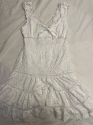 Vit spetsklänning från Gina Tricot - Superfin vit klänning från Gina Tricot i spets med volangdetaljer och söt rosett framtill. Klänningen är ärmlös med breda axelband och är perfekt för skolavslutningen, sommardagar och speciella tillfällen.