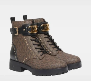 Skor från Michael Kors (40) - Helt nya och oanvända. Köpta från Best Secret för ca 2000kr. Skolådan medföljer! True to size! Snygga bruna boots med MK-monogram, svarta detaljer och guldfärgade metalldetaljer. Kraftig sula, snörning framtill och dekorativt spänne med logga. Guldnitar längs sidorna och svart hälparti i läderlook. Perfekta för en trendig streetstyle.
