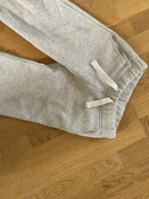 Ljusgrå mjukisbyxor XXS från Russemerch - Ljusgrå mjukisbyxor från Rut&Circle i storlek XXS. Byxorna har dragsko i midjan, två sidofickor och är gjorda i mjukt sweatshirtmaterial. Perfekta för en chill och avslappnad stil.