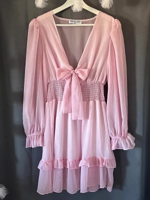 Rosa klänning - Supersöt ljusrosa kortklänning från Design by Amor med volanger och knytning framtill. Helt perfekt till skolavslutning eller bara sommaren överlag!💗🌸