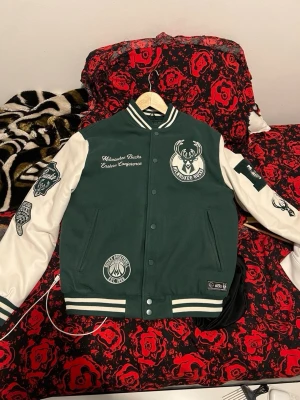 Milwaukee Bucks grön och vit bomberjacka - Snygg bomberjacka med Milwaukee Bucks-logga och broderade patches. Jackan är grön med vita ärmar, har ribbade muddar och knappar framtill. Perfekt för basketfans som vill sticka ut med coola detaljer och sportig stil.  (Har använts 4-5 gånger och är limited edition!!)