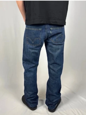 Blå raka jeans från Levi's - Säljer ett par klassiska blå jeans från Levi's med raka ben och tydliga sömmar på bakfickorna. Jeansen har normal midja och är tillverkade i slitstark denim. Perfekta för en avslappnad och tidlös stil.