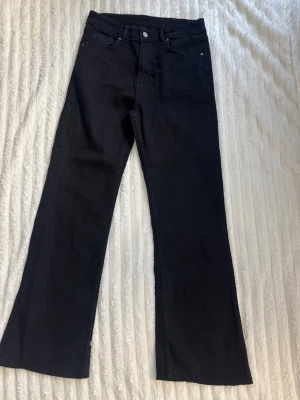 Svarta bootcut jeans - Säljer ett par svarta bootcut jeans med klassisk femficksdesign och silverfärgad knapp. Jeansen har raka ben med lätt utsvängning och är tillverkade i ett mjukt denimtyg. Perfekta för dig som gillar en tidlös och cool look.