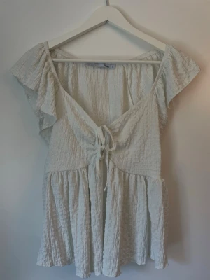 En vit och blå topp med volang och snörning  - Supersöta vit och blå topp i skrynklig bomull med volanger och v-ringning. Topparna har knyt framtill och en flowy passform som ger en avslappnad vibe. Perfekt för varma dagar och sommarhäng.