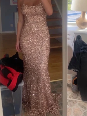 Glittrig långklänning med öppen rygg - NYPRIS 5000kr! Säljer en glittrig långklänning i champagnefärg med smala axelband och öppen rygg. Klänningen har figurnära passform och är täckt av paljetter som ger ett lyxigt intryck. Perfekt för dig som vill sticka ut på bal eller fest. Köptes i dressroom från märket Alessia!