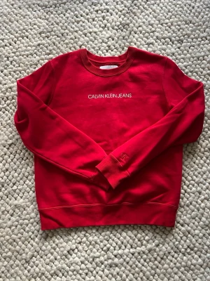 Röd sweatshirt från Calvin Klein Jeans -  röd sweatshirt från Calvin Klein Jeans med vit logotyp på bröstet och CK-broderi på ärmen.  Använd  fåtal gånger 