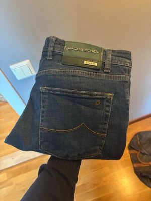 Mörkblå jeans från Jacob Cohen - Snygga mörkblå jeans från Jacob Cohen med klassisk femficksdesign och diskreta kontrastsömmar. Jeansen har normal passform och är tillverkade i mjuk bomull som ger en skön känsla hela dagen. Perfekta för dig som gillar stilrena och tidlösa plagg.