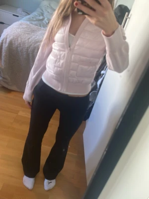 Ljusrosa dunväst med dragkedja - Säljer en ljusrosa dunväst med dragkedja framtill och quiltade paneler. Västen har en figurnära passform och är tillverkad i ett glansigt material. Perfekt att bära över en långärmad tröja för en snygg och sportig look.