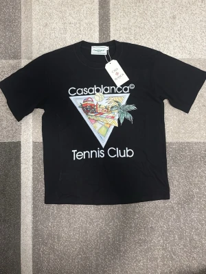 Svart Casablanca Tennis Club t-shirt - Snygg svart t-shirt från Casablanca med färgglatt tryck och texten 'Tennis Club' på framsidan. Klassisk passform och rund hals. Perfekt för dig som vill ha en trendig och sportig vibe på sommaren 