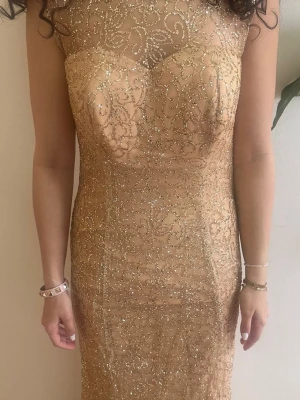 Glittrig långklänning i champagne - Elegant långklänning i champagnefärg med glittrigt mönster och figurnära passform. Klänningen har rund halsringning och är ärmlös, perfekt för speciella tillfällen. Dragkedja bak för enkel påklädning.