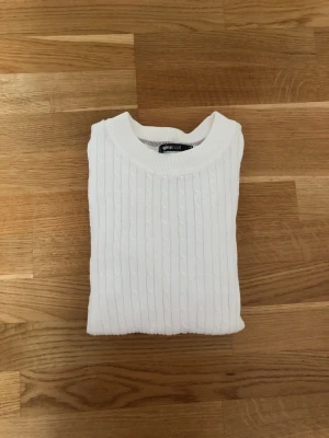 Vit kabelstickad tröja Gina Tricot - Säljer en vit kabelstickad tröja från Gina Tricot med rund halsringning och långa ärmar. Tröjan har ett klassiskt stickat mönster och är gjord i mjukt och stretchigt material som passar perfekt till en avslappnad stil. 100% ekologisk bomull. Helt ny, aldrig använd
