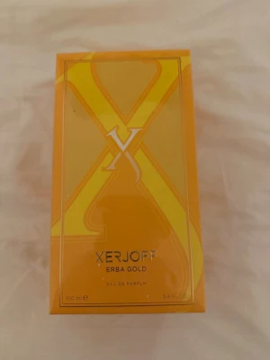 Xerjoff Erba Gold Eau de Parfum 100ml - Xerjoff Erba Gold Eau de Parfum i en snygg, rektangulär orange kartong med guldiga detaljer och stor X-logga. Förpackningen rymmer 100 ml och har en lyxig känsla som passar dig som gillar exklusiva dofter.