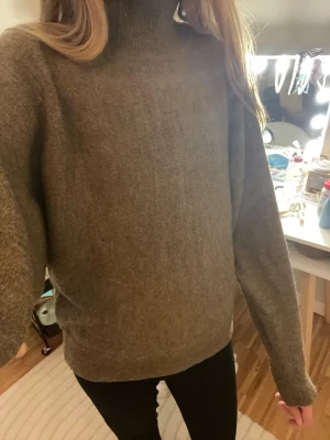 Brun stickad halv polotröja - Mysig brun stickad halv polotröja med avslappnad passform och långa ärmar. Tröjan har en hög krage och är tillverkad i ett mjukt material som känns skönt mot huden. Perfekt för kyliga dagar och enkel att styla med jeans eller kjol. Stickad på tvären.