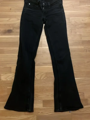 Svarta bootcut jeans - Säljer ett par svarta bootcut jeans med klassisk femficksdesign och utsvängda ben. Jeansen har knapp och dragkedja framtill samt bakfickor. Perfekta för dig som gillar en retrostil och vill ha ett par jeans som sticker ut. Smutsigt i ena fickan som tyvärr inte går bort (tror jag).!!