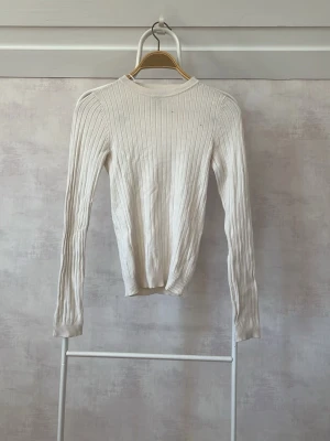 Vit ribbstickad tröja - Säljer en stilren vit ribbstickad tröja med rund hals och långa ärmar. Tröjan har en smal passform och är tillverkad i ett mjukt, stretchigt material som sitter snyggt på kroppen. Perfekt att matcha med jeans eller kjol.