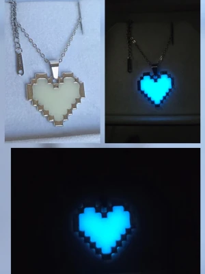 Pixelhjärta Glow in the dark hjärthalsband - Unikt handgjort halsband med ett pixelhjärta som lyser i mörkret. Hängsmycket är vitt i dagsljus och får en cool blå glow när det är mörkt. Kedjan är i silverfärgad rostfritt stål. Perfekt accessoar för dig som gillar gaming eller retrostil. Hänget börjar lysa i mörker efter att ha varit en kort stund i vanligt dagsljus eller solljus. Lyser vanligtvis i flera timmar. Tål vatten, missfärgas inte och har en lång livslängd. 