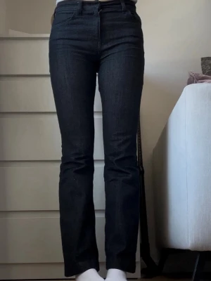 Mörkblå raka jeans med hög midja - Säljer ett par mörkblå jeans med rak passform och hög midja. Jeansen har klassiska fem fickor och är tillverkade i ett stretchigt denim-material som sitter snyggt. Perfekta för dig som gillar en tidlös och enkel stil. Jag är 180cm och de är lite för korta för mig.