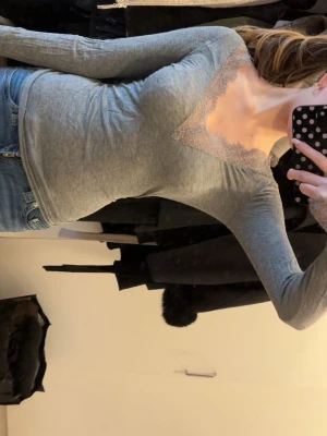 Intimissimi tröja - Säljer en grå långärmad topp med v-ringning och snygg spetsdetalj runt halsen. Perfekt att matcha med jeans eller kjol för en cool look. Toppens passform är slim och materialet känns mjukt och bekvämt.