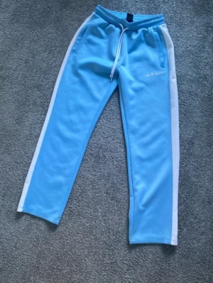 Blå mjukisbyxor med vita detaljer Palm angels - Snygga ljusblå mjukisbyxor med vita sidoremsor och dragsko i midjan. Byxorna har raka ben och två fickor framtill. Perfekta för en avslappnad och sportig look.