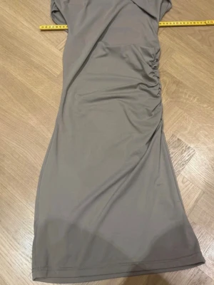 Beige långklänning från SHEIN - Stilren beige långklänning från SHEIN i mjukt och stretchigt polyestermaterial med elastan. Klänningen har en åtsittande passform och snygg rynkdetalj på sidan som ger en modern look. Perfekt för dig som gillar minimalistisk stil.