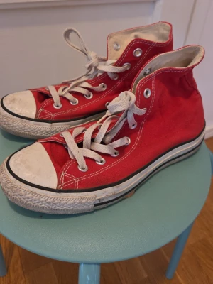 Röda Converse All Star Highs - Klassiska röda Converse All Star high-top sneakers med vit tå och sula, vita snören och metallöljetter. Skorna har den ikoniska All Star-loggan på sidan och är tillverkade i slitstark canvas. Perfekta för en avslappnad och cool stil.