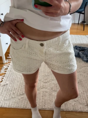 Vita spetsdetaljerade shorts - Säljer ett par vita shorts med snygga spetsdetaljer framtill. Shortsen har knapp och dragkedja samt bälteshällor. Shortsen har en jätteliten fläck på baksidan, men inget som man lägger märke till (visar på sista bilden). Storlek 38🌸🌸