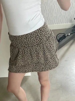 Leopardmönstrad volangkjol - Säljer en kort kjol med leopardmönster och dubbla volanger. Kjolen har bred midja och är i mjukt, lätt material som ger en skön passform. Perfekt för dig som vill sticka ut med ett trendigt djurmönster.
